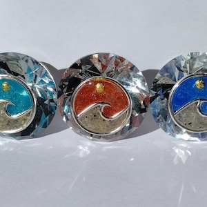 May include: Three crystal paperweights with a wave design inside. The wave is surrounded by sand and a small sun. The paperweights are blue, orange, and blue.