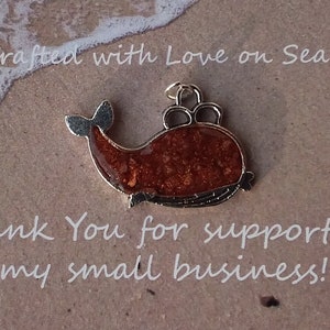 May include: A small, brown whale charm with a silver finish. The whale is filled with glittery, brown resin. The charm is on a brown background with the text "Handcrafted with Love on Sea Street" and "Thank You for supporting my small business!"