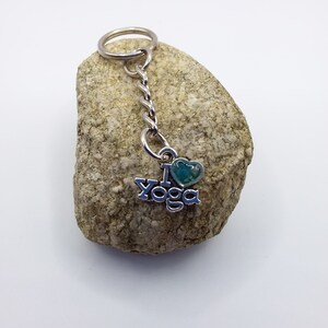 May include: A silver keychain with a heart charm and the words "I love Yoga" on it. The keychain is on a small rock.