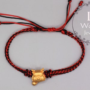May include: Red and black braided string bracelet with a gold charm in the shape of a dragon's head.