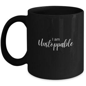 May include: Black ceramic coffee mug with a white inscription that reads "I am Unstoppable".