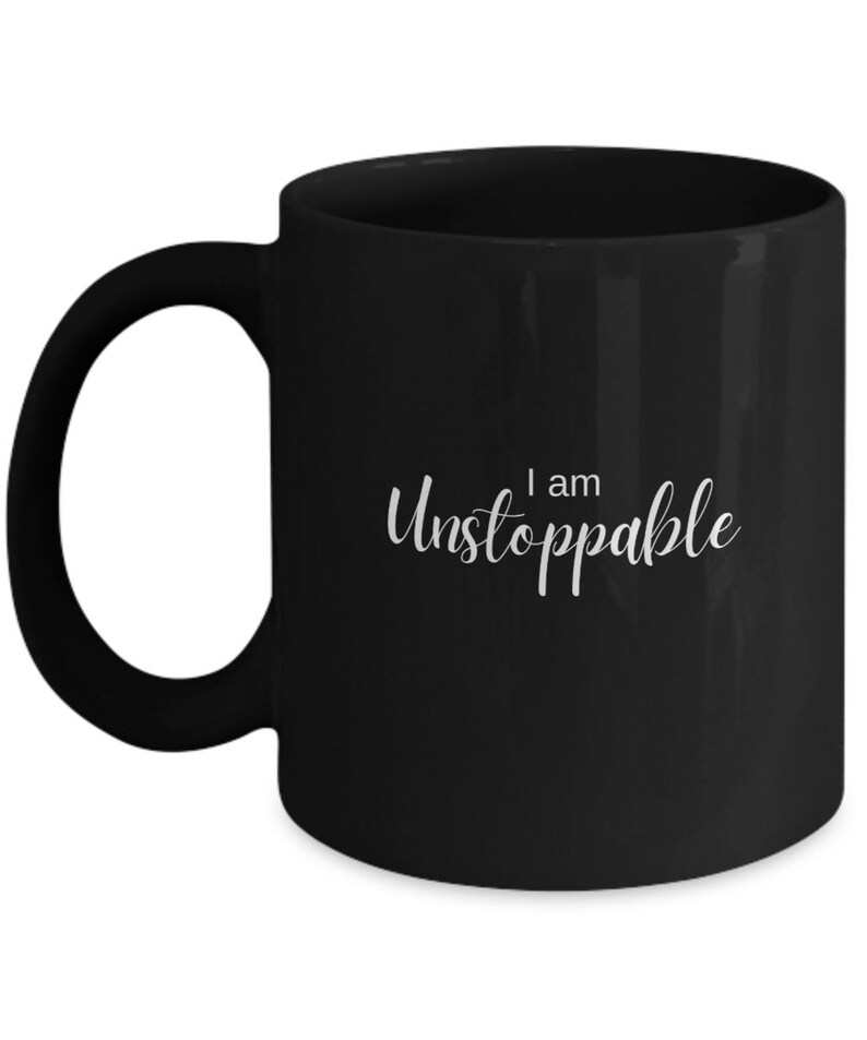 May include: Black ceramic coffee mug with a white inscription that reads "I am Unstoppable".