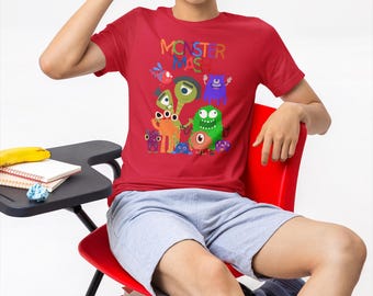 May include: Red t-shirt with the text "MONSTER MAS" and colorful cartoon monster graphics. The person is wearing light blue shorts and white socks. The person is sitting on a red chair.