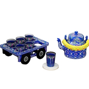 Op de afbeelding: Een blauwe, beschilderde houten kar met zes glazen en een bijpassende blauwe, beschilderde metalen theepot met een gele handgreep. De kar heeft vier wielen en is versierd met kleurrijke bloemenpatronen.