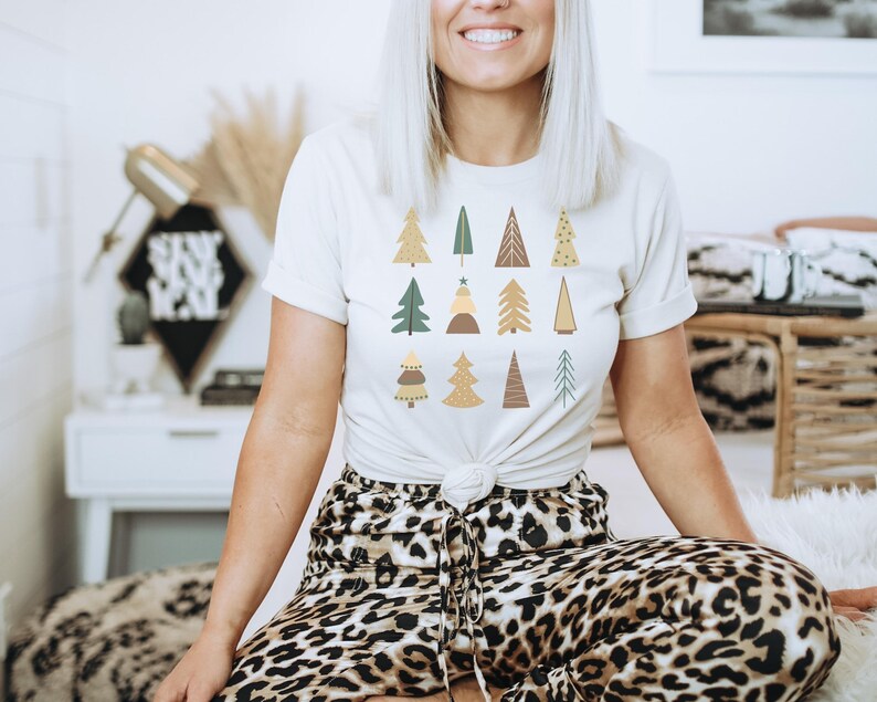 May include: A white t-shirt with a pattern of stylized Christmas trees in shades of green, brown, and yellow. The trees are decorated with stars and dots.