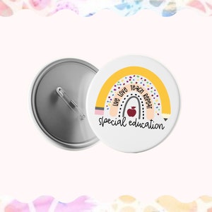 May include: A white button with a yellow rainbow design and the text "Live Love Teach Repeat Special Education". The rainbow has a pencil design on each end and a red apple in the center.