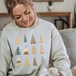 May include: A light beige sweatshirt with a pattern of stylized Christmas trees in shades of green, yellow, and brown.