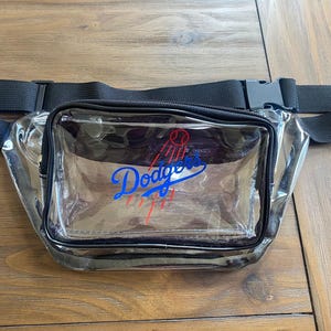 Pu&ograve; includere: Marsupio trasparente con cinturino e fibbia neri regolabili. La parte anteriore del marsupio presenta il logo dei Los Angeles Dodgers in blu, rosso e bianco.