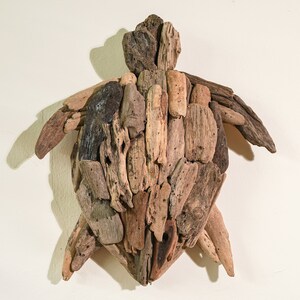 May include: A wall-mounted sculpture of a turtle made from driftwood. The turtle is made of many pieces of wood, all different shapes and sizes, and is painted in shades of brown and gray.