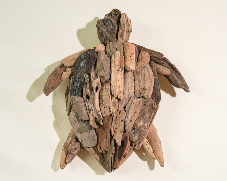 May include: A wall-mounted sculpture of a turtle made from driftwood. The turtle is made of many pieces of wood, all different shapes and sizes, and is painted in shades of brown and gray.