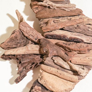 May include: A crescent moon-shaped wall decor made from driftwood. The wood is arranged in a layered pattern, creating a textured and organic look.