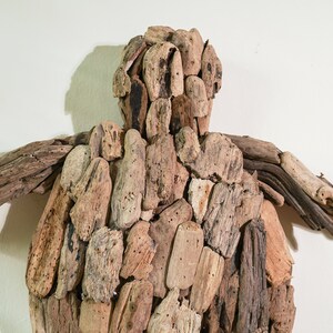 May include: A wall sculpture made of driftwood, shaped like a turtle. The sculpture is made of many pieces of driftwood, all different sizes and shapes. The driftwood is a natural brown color.