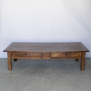 May include: A rectangular low coffee table crafted from dark brown wood with a smooth, flat top surface. The table features four sturdy legs and two horizontal drawers positioned side by side, each equipped with a small, round wooden knob handle.