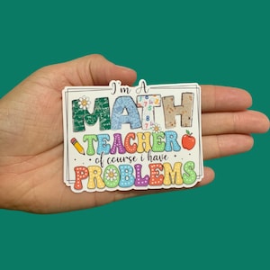 May include: A colorful sticker with the text "I'm a Math Teacher, of course I have Problems". The text is surrounded by a white border and decorated with colorful numbers, a pencil, a daisy, and an apple.