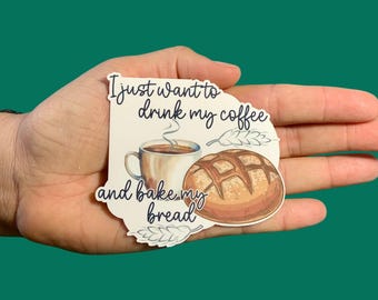 May include: A sticker with the text "I just want to drink my coffee and bake my bread." The sticker features a coffee cup, a loaf of bread, and wheat sprigs. The sticker is held in a hand against a teal background.