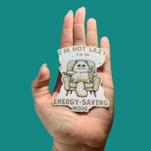 May include: A sticker featuring a cartoon cat in a recliner holding a remote and a drink. The cat has fluffy white fur and is wearing sunglasses. Text on the sticker reads "I'M NOT LAZY I'M IN ENERGY-SAVING MODE."