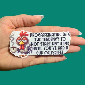 May include: A white sticker with a cartoon rooster holding a cup of coffee. The sticker says "Procaffeinating (N.): The tendency to not start anything until you've had a cup of coffee."