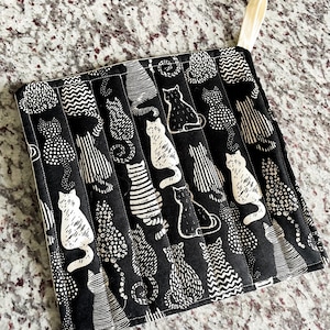 May include: Black and white pot holder with a cat pattern. The pot holder is quilted and has a loop for hanging.