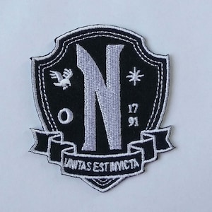 Könnte beinhalten: Schwarzer und weißer gestickter Patch in Form eines Schildes. Der Schild zeigt einen großen weißen Buchstaben "N" in der Mitte, einen weißen Vogel mit ausgebreiteten Flügeln, einen weißen Stern und den Text "17 91". Ein weißes Band am unteren Rand des Schildes trägt die Aufschrift "Lunitas Est Invicta".