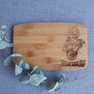 May include: A wooden cutting board with a laser-engraved image of a character from the anime Dragon Ball Z. The character is holding a sphere with stars on it. The text "Dragon Ball Z" is engraved below the image.