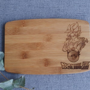 May include: A wooden cutting board with a laser-engraved image of a character from the anime Dragon Ball Z. The character is in a fighting pose with a dragon ball in their hand. The text "Dragon Ball Z" is engraved below the image.