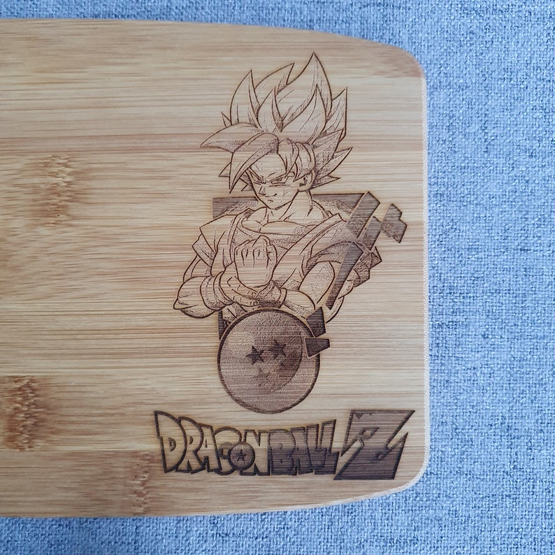 May include: A wooden cutting board with a laser-engraved image of a character from the anime Dragon Ball Z. The character is standing with their arms crossed and has a serious expression. The image is surrounded by the text "Dragon Ball Z".