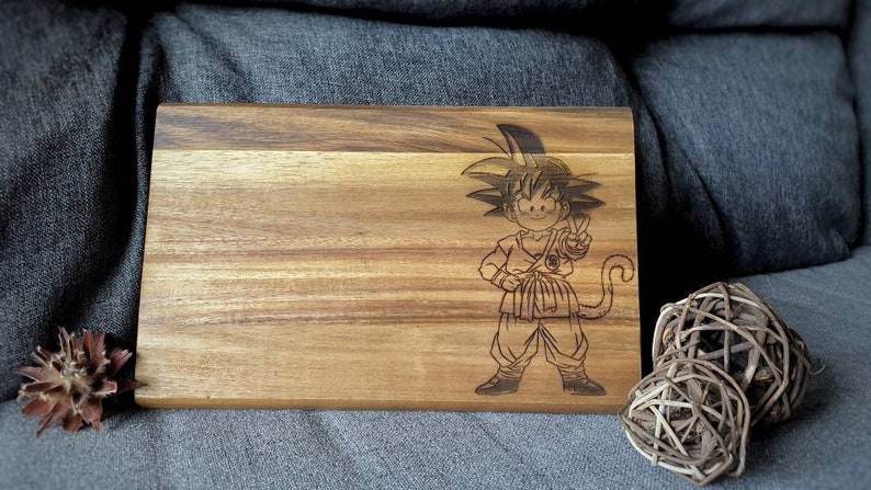 May include: A wooden cutting board with a laser-engraved image of a cartoon character with spiky black hair. The character is wearing a dark-colored outfit with a belt and has a tail.
