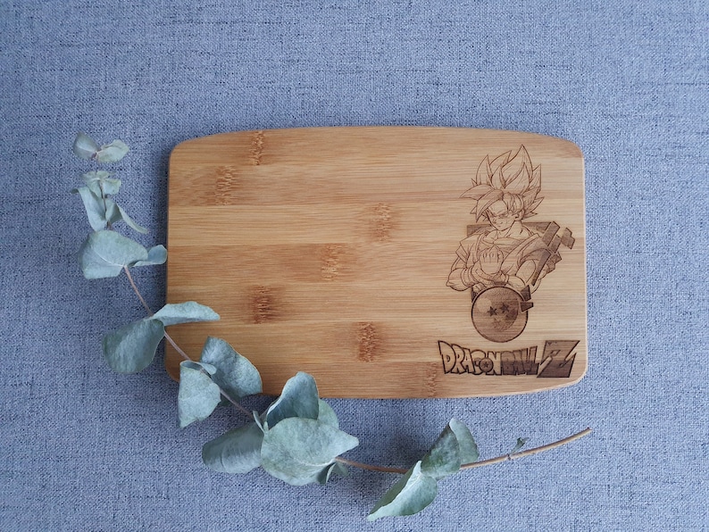 May include: A wooden cutting board with a laser-engraved image of a character from the anime Dragon Ball Z. The character is holding a sphere with stars on it. The text "Dragon Ball Z" is engraved below the image.