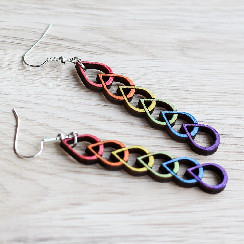 Earrings made of wood with hand painted metallic rainbow accents. The earrings have a slender, linked raindrop design. Each raindrop is painted a different colour. From top to bottom the colours are: red, orange, yellow, green, blue, violet.