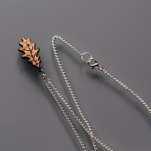 Oak leaf pendant necklace close up on grey background. The chain is a thin, silver plated curb chain with a lobster clasp and large linking ring for easy attachment.