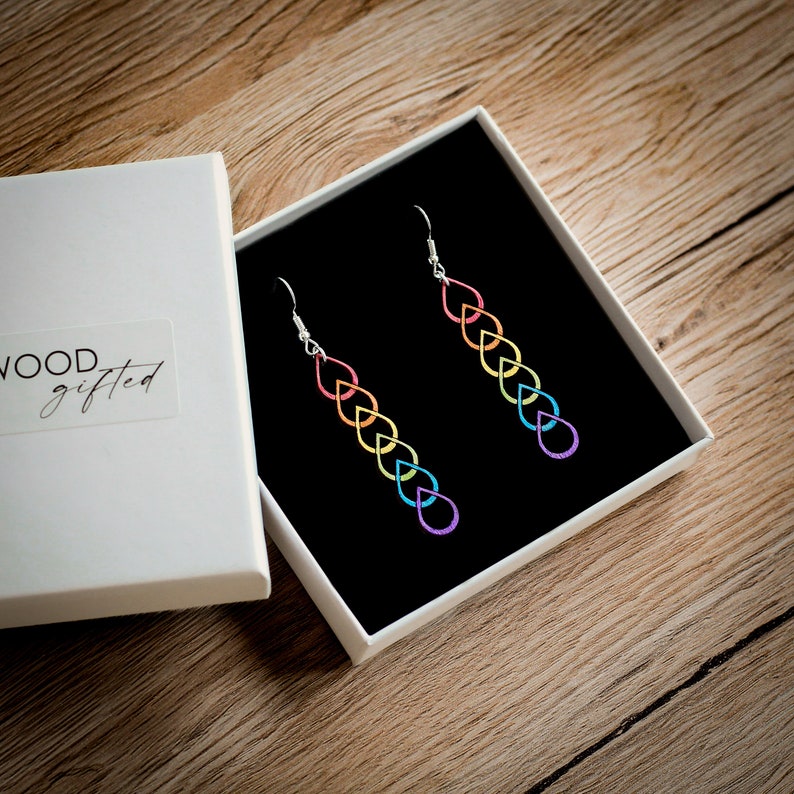 Hand painted wooden earrings in a gift box. The gift box is an attractive, white square box and the earring sit inside on a foam black pillow. The box sits on a wood table.