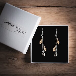 Dangly natured inspired earrings in a gift box. The gift box is square and white. The earrings are placed inside on a foam black pillow.