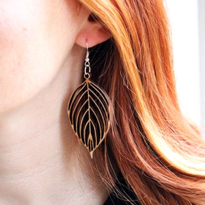Woman wearing wooden leaf earrings. The earrings are made from light wood and hand from the ear with silver hooks.