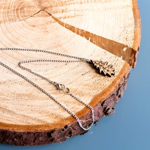 Oak leaf pendant, engraved and carved into oak wood. Attached to silver plated chain and displayed on a log slice.