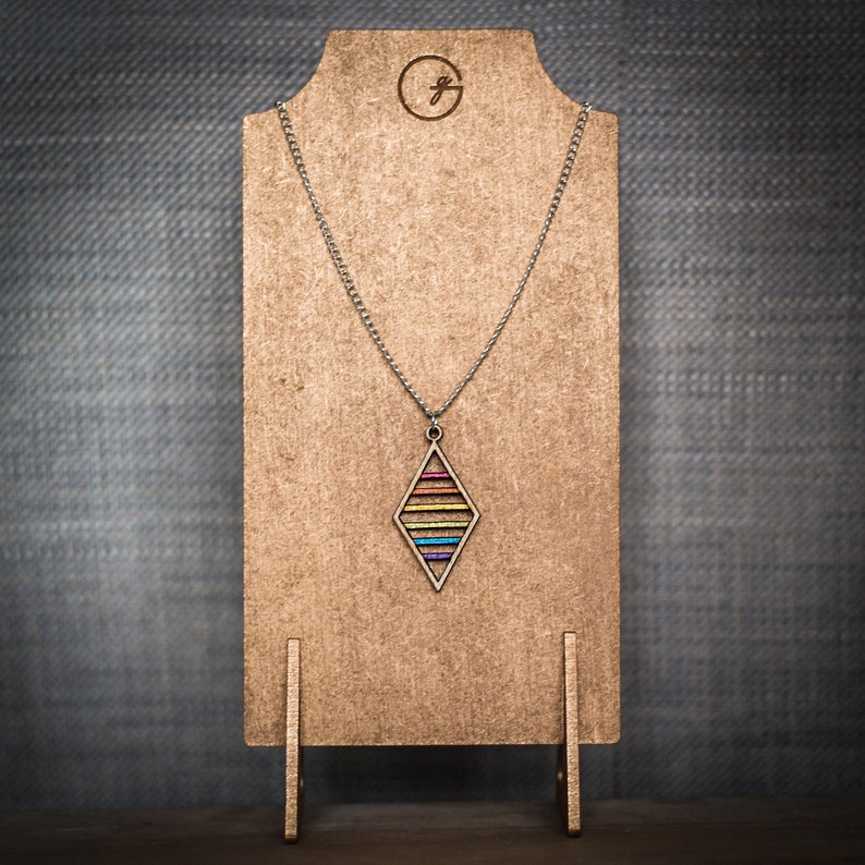 Rainbow stripe pendant on a silver chain which is draped across a golden necklace stand. The pendant is wooden and has 6 floating bars set within a diamond shaped frame.