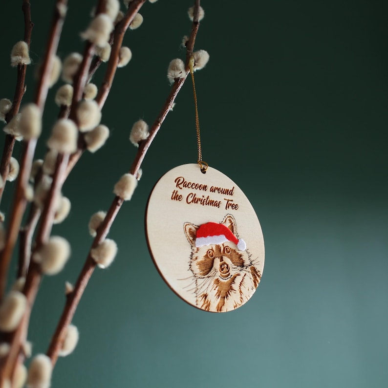 Side view of hanging raccoon ornament, displayed against green background. A mix of texture and layers add interest to this handcrafted, original piece designed and made by a small business based in the UK.
