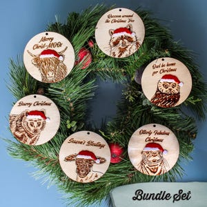 Bundle set of 6 animal Christmas tree ornaments. The ornaments are displayed on a wreath. Each one is made from wood and has an animal themed engraving with a velvet touch hat & accompanying pun.