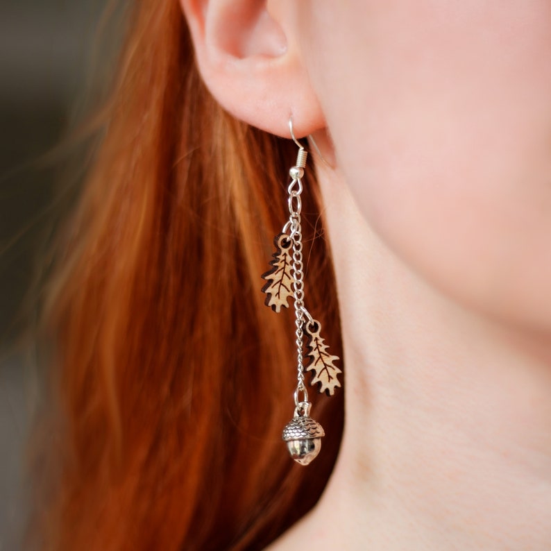 Woman with red hair wearing drop earrings. The dangly earrings have wooden oak leaf charms that dangle from a silver chain with a silver acorn charm at the bottom.