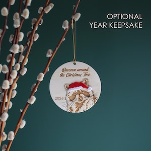 Showing the raccoon ornament handing from a branch, this variation is also engraved with the year.