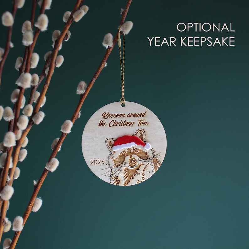 Showing the raccoon ornament handing from a branch, this variation is also engraved with the year.