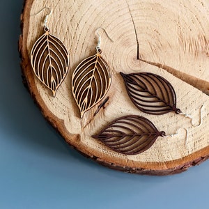 Wooden leaf earrings on log slice. One pair is made from light wood and the other is made from dark wood.