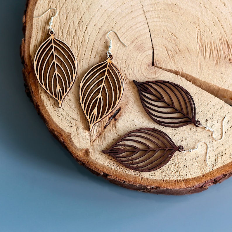 Wooden leaf earrings on log slice. One pair is made from light wood and the other is made from dark wood.