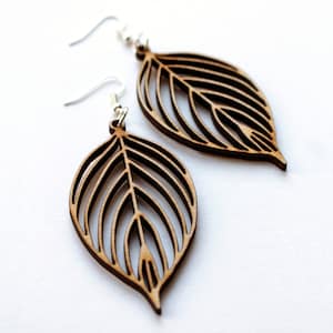 Detail shot of wooden leaf earrings with silver hooks on white background. The wood is a skeleton leaf shape. It is birch wood so is light in colour except along the cut edges which are dark brown.