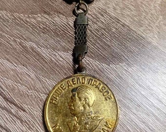 May include: Vintage gold-toned metal keychain with a circular pendant. The pendant features a profile of a man and Cyrillic text. The keychain has a ring and a chain-like detail connecting the pendant.