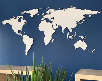 Op de afbeelding: Een witte houten wereldkaart uitsnijding gemonteerd op een donkerblauwe muur. De kaart is een eenvoudige omtrek van de continenten en oceanen. Een groene plant bevindt zich op de voorgrond.