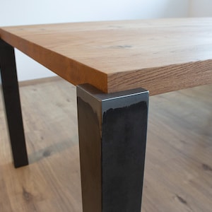 Könnte beinhalten: Eine Tischplatte aus Holz mit einer dunkelbraunen Oberfläche sitzt auf schwarzen Metallbeinen. Die Tischplatte hat eine natürliche Holzmaserung.