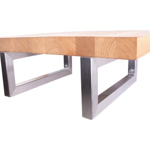 Könnte beinhalten: Ein Holz-Couchtisch mit einer natürlichen Holzoptik und Edelstahlbeinen. Der Tisch hat eine rechteckige Tischplatte und die Beine sind abgewinkelt.
