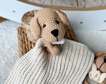 May include: A crocheted beige puppy toy with black eyes and a black nose, lying on a cream crocheted blanket.
