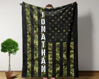May include: A black and green fleece blanket with a camouflage pattern and the American flag. The name "JONATHAN" is printed vertically on the left side of the blanket.