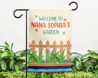 May include: A welcome garden flag with a brown wooden fence, green grass, and pink flowers. The text on the flag reads "Welcome to Nana Sophia's Garden".